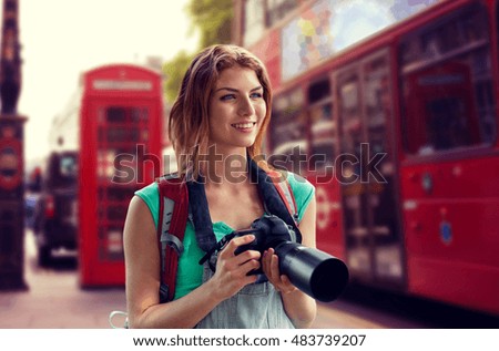 travel, tourism and people concept - happy young woman with backpack and camera photographing over london city street background
