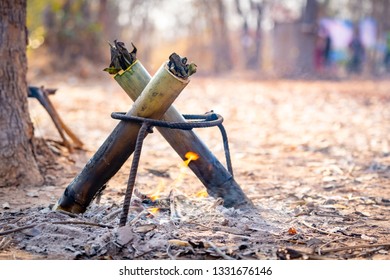 Travel Tourist Forest Concept, Cooking In Bamboo Tube Section For Roast Or Grill On Hills In Camping. Fire Flame Burning To Heat Bamboo And Food By Grill. This Cooking Is Traditional In Countryside.