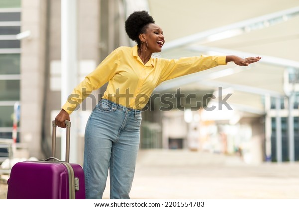 Travel And\
Transportation. Happy African American Woman Hailing A Taxi Cab\
Standing With Suitcase Looking Aside Posing Near Airport Terminal\
Outdoors. Taxi Service Advertisement\
Concept.