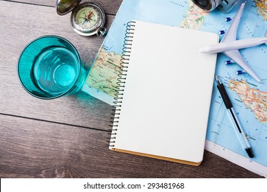 travel , trip vacation, tourism  mockup - close up of compass, glass of water note pad, pen and toy airplane and touristic map on wooden table. Empty space you can place your text or information.