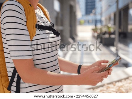 travel to United Arab Emirates, young asian female traveler with backpack and hat in big city of Abu Dhabi, using app on smartphone, chating with friends. Vacation and tourist destination concept.
