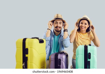 Travel vacation, preparation for rest on beach. Happy smiling traveler couple wearing summer hat looking at camera sitting with packed luggage suitcase. Headshot studio portrait on grey background