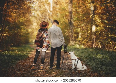 Travel and Wanderlust. Stylish couple standing with cute dog in sunny autumn woods. Young  hipster family hiking with swiss shepherd white dog. Traveling with pet, loyal companion.
