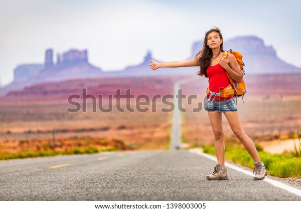 Travel woman backpacking hitchhiking on road\
trip hitching a ride from car in amazing landscape nature. Arizona,\
Utah, USA. Summer vacation\
adventure.