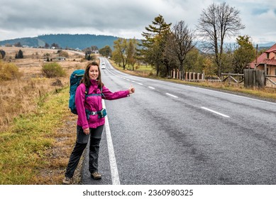 Travel woman hitchhiking. Beautiful young female hitchhiker by the road during mountain trip. Travel and vacation theme - Powered by Shutterstock