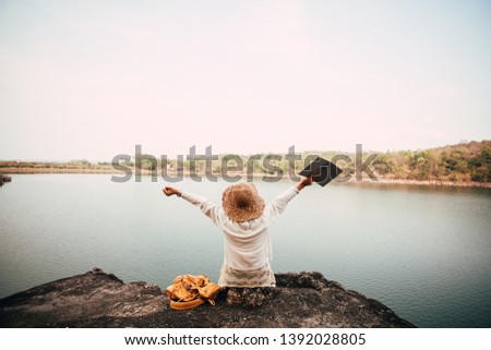 Travel Woman sitting on rocks and reading a book with landscape on the background 