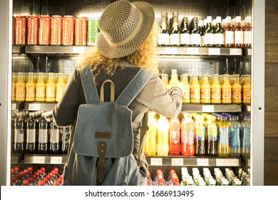 Travel woman viewed from back choosinf beverage in a fresh fridge - airport or station bar concept and traveler passenger choosing drinks - modern lifestyle backpack people buying drinks bottles