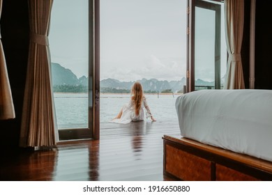Travel Woman in White Dress Sitting Outdoor near Wooden House on Water. View on Tourist Woman Relaxing and Leisure from Raft House on Cheow Lan Lake in Thailand. Eco Tourism