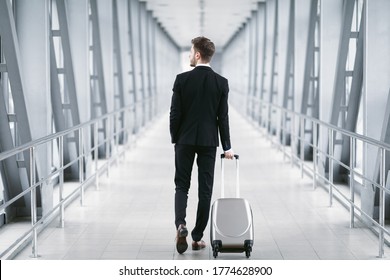 Travel To Work. Back view of business man in suit dragging suitcase luggage bag in the airport, copyspace - Powered by Shutterstock