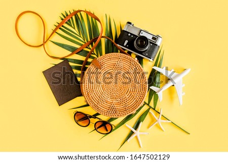 Traveler accessories concept on yellow background. Fashionable handmade natural round rattan bag, retro camera and tropical leaves. Stylish eco bamboo bag. Summer fashion concept. 