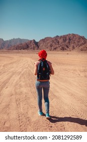 Traveler Admiring Sinai Desert And Mountains. Tourist Woman With Backpack Wearing Scarf On Head Walking On Sand. Summer Winter Vacation