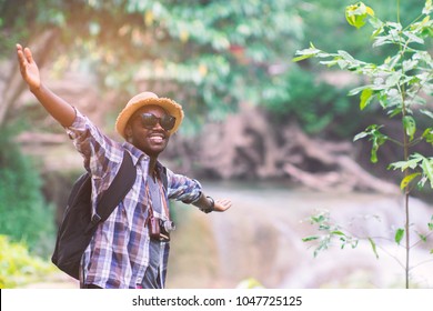 Traveler african american man with backpack holding camera with green natural background.