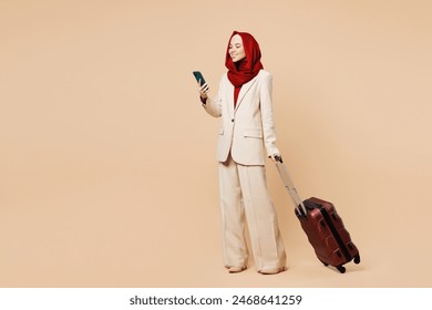 Traveler Asian Muslim woman wears red abaya hijab hold suitcase bag mobile cell phone isolated on plain beige background Tourist travel abroad in free time rest getaway. Air flight trip, UAE concept - Powered by Shutterstock