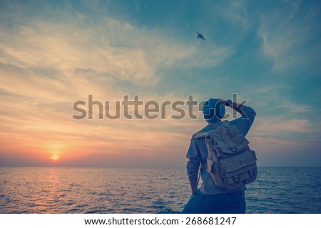 traveler with backpack on the rocks near the sea looking far away at airplane (intentional vintage color)
