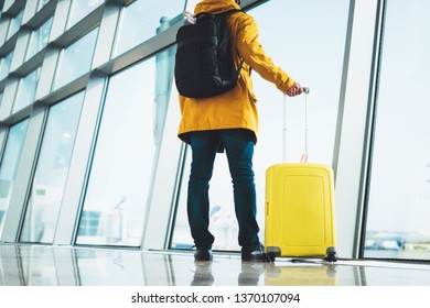 traveler in bright jacket with yellow suitcase backpack at airport on background large window blue sky, passenger waiting flight in departure hall of lobby terminal lounge area, vacation trip concept - Shutterstock ID 1370107094