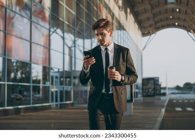 Traveler businessman young man in black suit going walk outside at international airport terminal use mobile phone book taxi order hotel hold paper cup coffee to go Air flight business trip concept. - Powered by Shutterstock