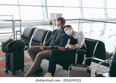 Traveler Couple In Pandemic Waiting At Airport Terminal. Man And Woman In Face Masks Sitting At Airport Waiting Area.