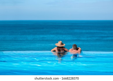 Traveler couple with sunhats hugging in a infinity pool and enjoyinf the view to the mediterranean sea