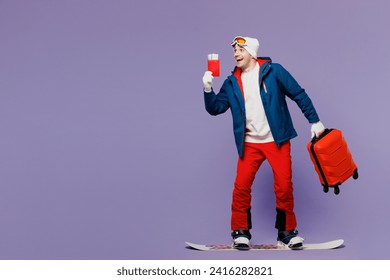 Traveler excited man wear blue windbreaker jacket ski goggles mask hat hold passport ticket bag snowboarding isolated on plain purple background. Tourist travel in free time rest. Air flight concept - Powered by Shutterstock