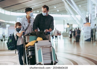 Traveler family wearing face mask with luggage trolley waiting at airport. Couple walking with their son at airport in pandemic.