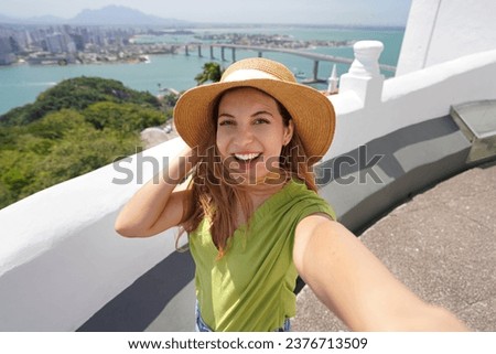 Traveler fashion smiling woman takes self portrait with the panoramic view of Vitoria City in the state of Espirito Santo, Brazil