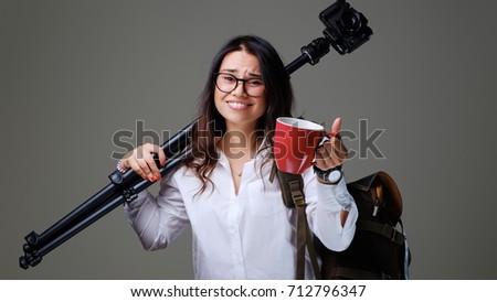 Traveler female holds digital photo camera and a red coffee cup over grey background.