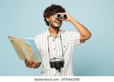 Traveler fun Indian man wear white casual clothes hold read map use binocular isolated on plain blue background. Tourist travel abroad in free spare time rest getaway. Air flight trip journey concept