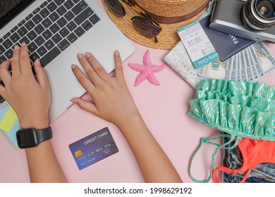 Traveler Getting Ready For A Trip, He Is Packing His Bag And Booking A Flight Online Using A Credit Card And A Laptop, Flat Lay. Planning Traveling Trip Notes. Travel Accessories On Pink Background.