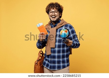 Traveler happy Indian boy IT student wear casual clothes hold passport ticket globe Earth map isolated on yellow background. Tourist travel abroad for studying at university. Air flight trip concept