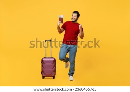 Traveler happy Indian man wear red casual clothes hold bag passport ticket isolated on plain yellow background. Tourist travel abroad in free spare time rest getaway. Air flight trip journey concept