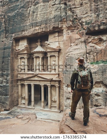 A traveler in a hat with a backpack looks at Al-Khazneh in Petra. Indiana Jones near the treasury in Petra. The best view of the main temple of Al-Khazneh in Petra, Jordan.