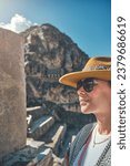Traveler hipster girl in hat with backpack exploring ruins of Ollantaytambo Ruins in Sacred Valley of Peru