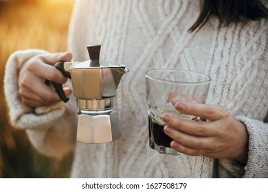 Traveler holding geyser coffee maker and glass cup with fresh coffee in sunny warm light in rural countryside herbs. Atmospheric rustic moment. Alternative coffee brewing in travel. - Shutterstock ID 1627508179