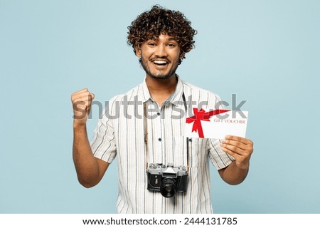 Traveler Indian man wear white casual clothes hold store gift coupon voucher card isolated on plain blue background. Tourist travel abroad in free spare time rest getaway. Air flight journey concept
