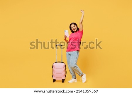 Traveler Indian woman wearing casual clothes hold suitcase passport ticket isolated on plain yellow background. Tourist travel abroad in free spare time rest getaway. Air flight trip journey concept