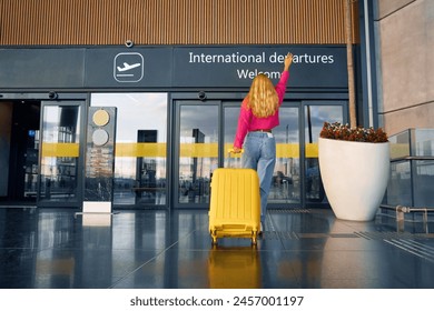 A traveler is late and runs into the international departures terminal. Joyfully raising her hand, the traveler runs with her suitcase. Back Low angle view - Powered by Shutterstock