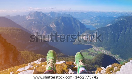 traveler legs in stylish green sneakers sitting on high alp mountain cliff enjoying scenery mountain top. Pov view Hiking freedom concept Austria Hallstatter See lake Krippenstein mountain Hallstatt 