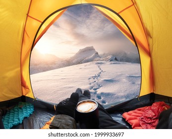 Traveler man holding coffee cup and enjoying the view of sunrise on snowy mountain inside a yellow tent - Powered by Shutterstock