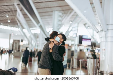 Traveler Man Hugging To Woman At Airport Arrival Gate. Woman In Face Mask Greeting Man After Arriving From Tour Post Pandemic.