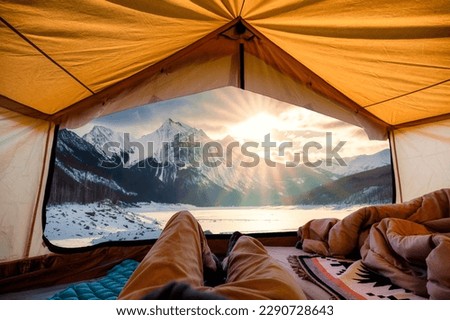 Traveler man relaxing inside a yellow tent with sunrise over Medicine Lake in winter at Jasper national park, AB, Canada