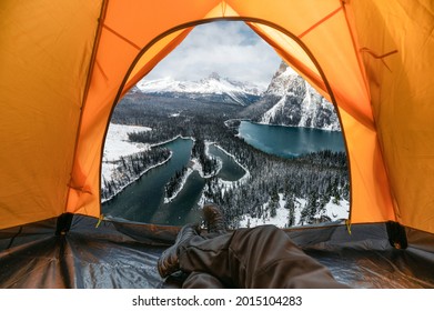 Traveler Man Resting And Enjoying View Of Snowy Mountain And Lake Inside A Orange Tent On Winter At Yoho National Park, Canada