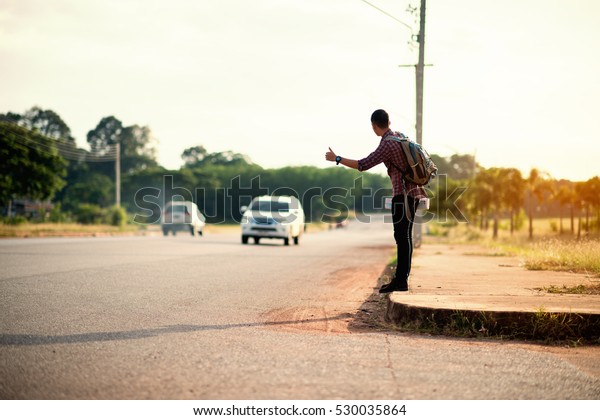 Traveler man waves a hand with attempt to stop the\
car on the road