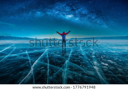 Traveler man wear red clothes and raising arm standing on natural breaking ice with milky way at Lake Baikal, Siberia, Russia.