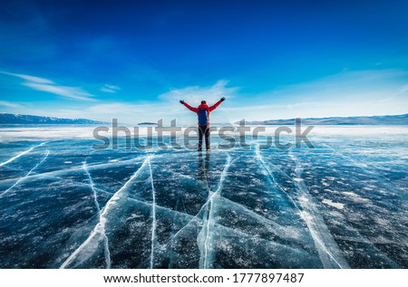 Traveler man wear red clothes and raising arm standing on natural breaking ice in frozen water at Lake Baikal, Siberia, Russia.