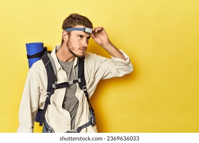 Traveler with mountain backpack, mat, and headlamp on yellow backdrop - Powered by Shutterstock