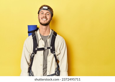 Traveler with mountain backpack, mat, and headlamp on yellow backdrop - Powered by Shutterstock