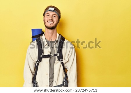 Traveler with mountain backpack, mat, and headlamp on yellow backdrop