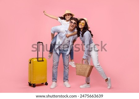 Traveler parents with child girl sit on father back, posing with suitcase isolated on pink background, ready to travel abroad in free time