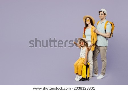 Traveler parents mom dad with child girl wear casual clothes hold bags point aside isolated on plain purple background. Tourist travel abroad in free time rest getaway. Air flight trip journey concept