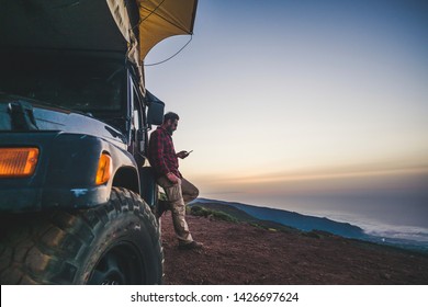 Traveler People With Car And Camping Concept - Lonely Man Use Cellular Phone To Connect To Internet Outside His Vehicle - Mountain And Nature Outdoor Around - Enjoying Freedom And Alternative Vacation